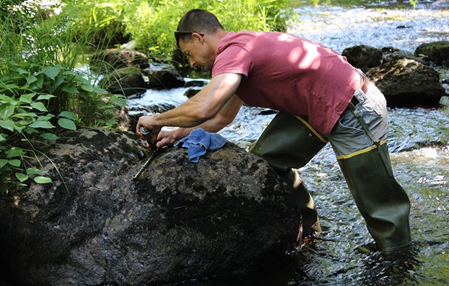 Man in waders adjusting a small instrument in the middle of a stream in Maine