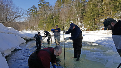 Men chipping choles in ice cover on a stream